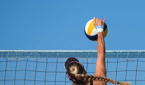A woman with a long braid jumps into the air to spike a volleyball