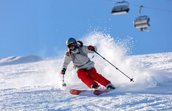 A woman skier in bright orange pants is skiing down a snowy slope