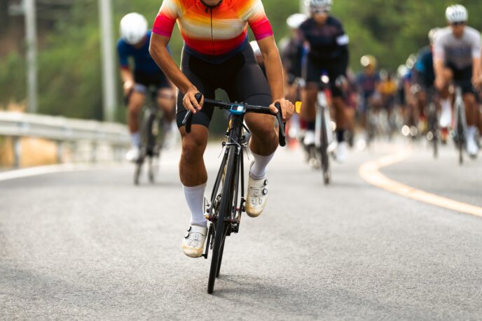 A man on a bike leads a pack of other riders, and we are focused in on his strong legs and knees.