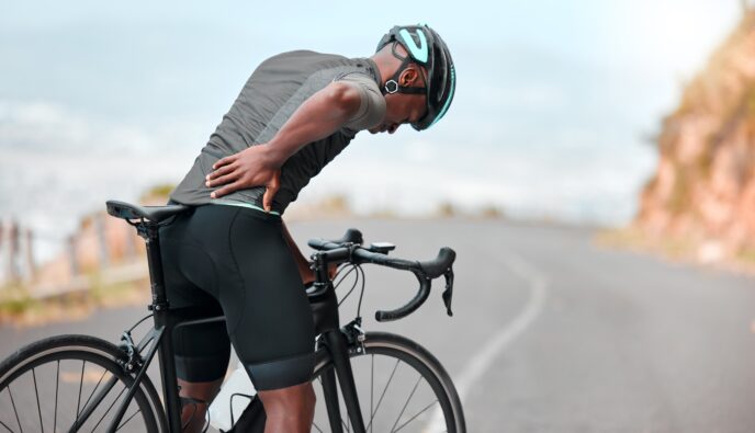 An athletic man on a bicycle holds his lower back area in pain.