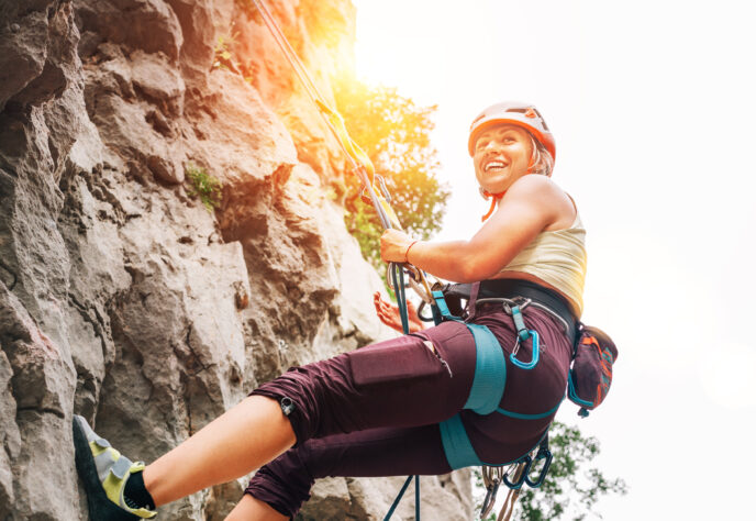 A woman scales a wall while smiling and holding on to a safety rope.