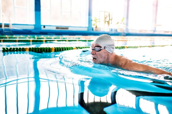An older man wearing googles in a swimming pool swimming laps