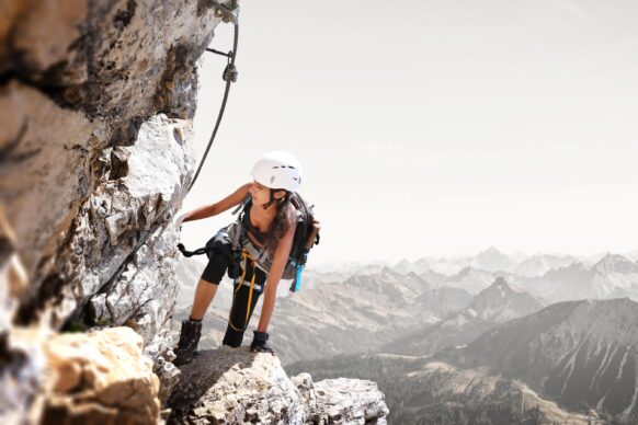 A young woman wearing a white helmet in the mountains, rock climbing.