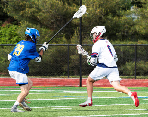 Two people are on a lacrosse field competing for the ball