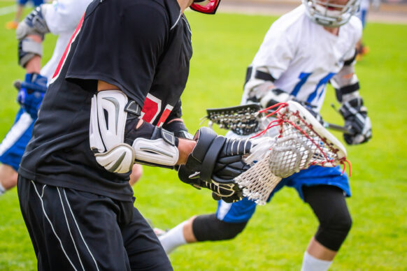 A young man in a dark jersey keeps possession of a lacrosse ball in his net.