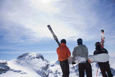 Skiers and a snowboarder on a mountain carrying their equipment