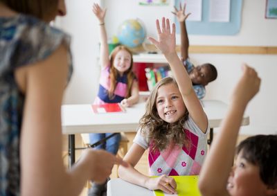 Kids in a class room raising their hands